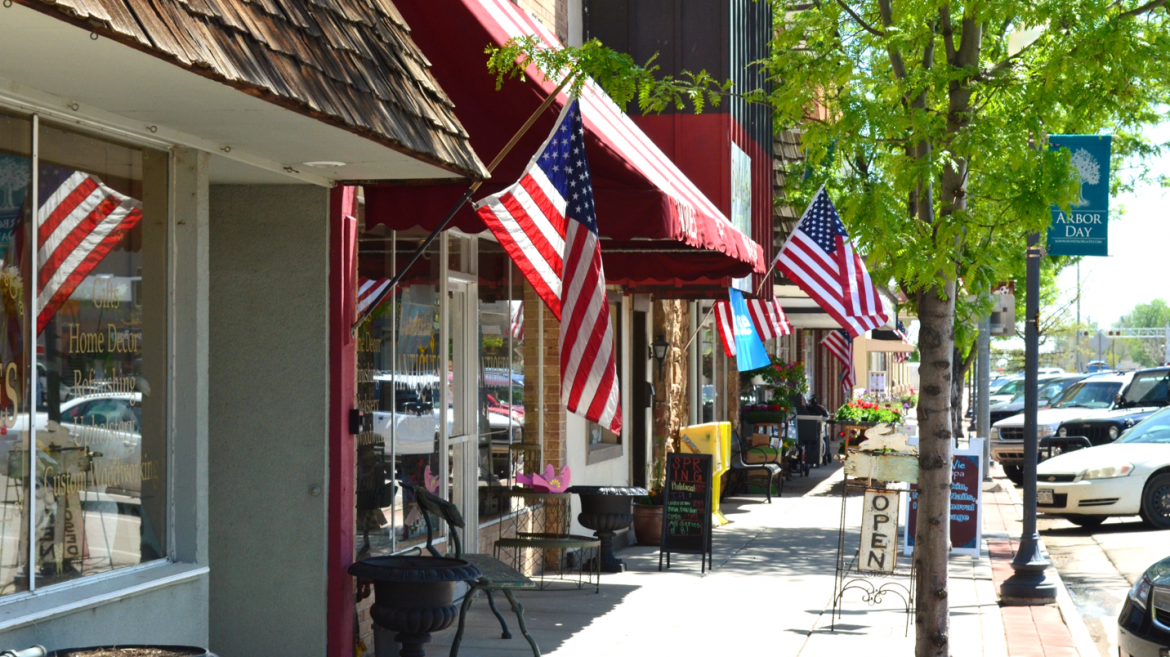A sunny street lined with shops and American flags; a sign celebrates Arbor Day.
