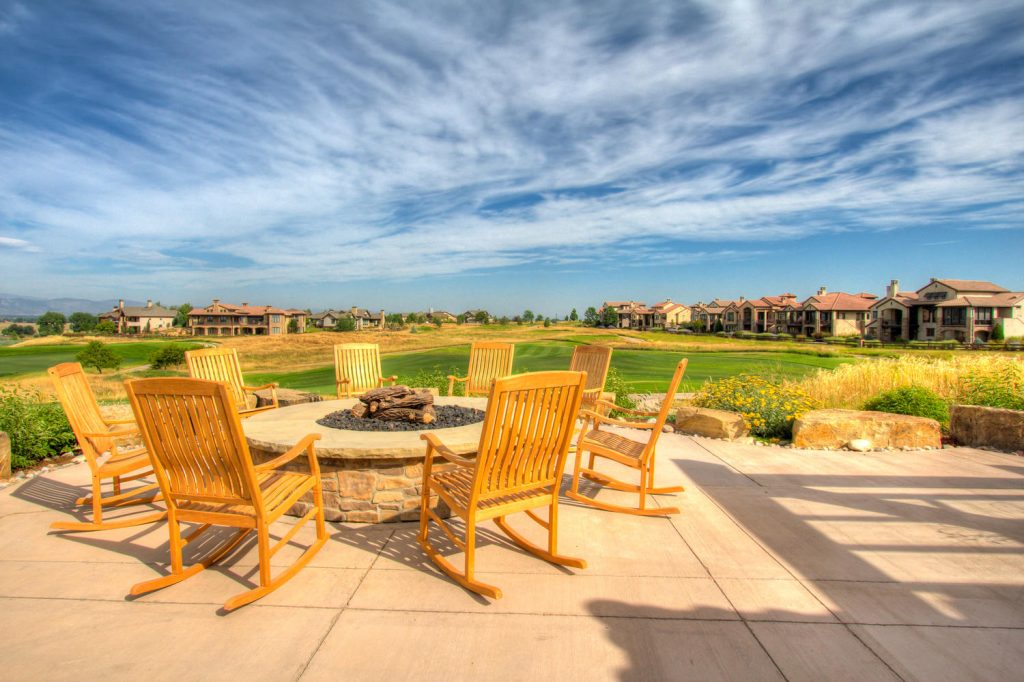 Patio with chairs around a fire pit overlooking a golf course and houses under a blue sky.
