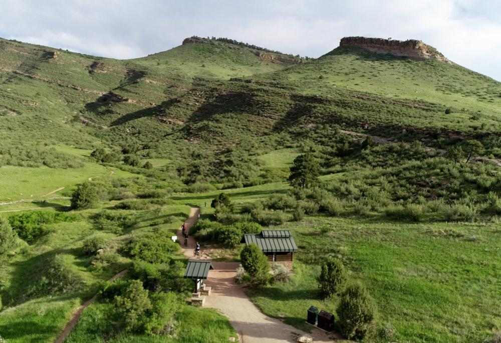 Green park with trails, shelters, and a hill in the background.