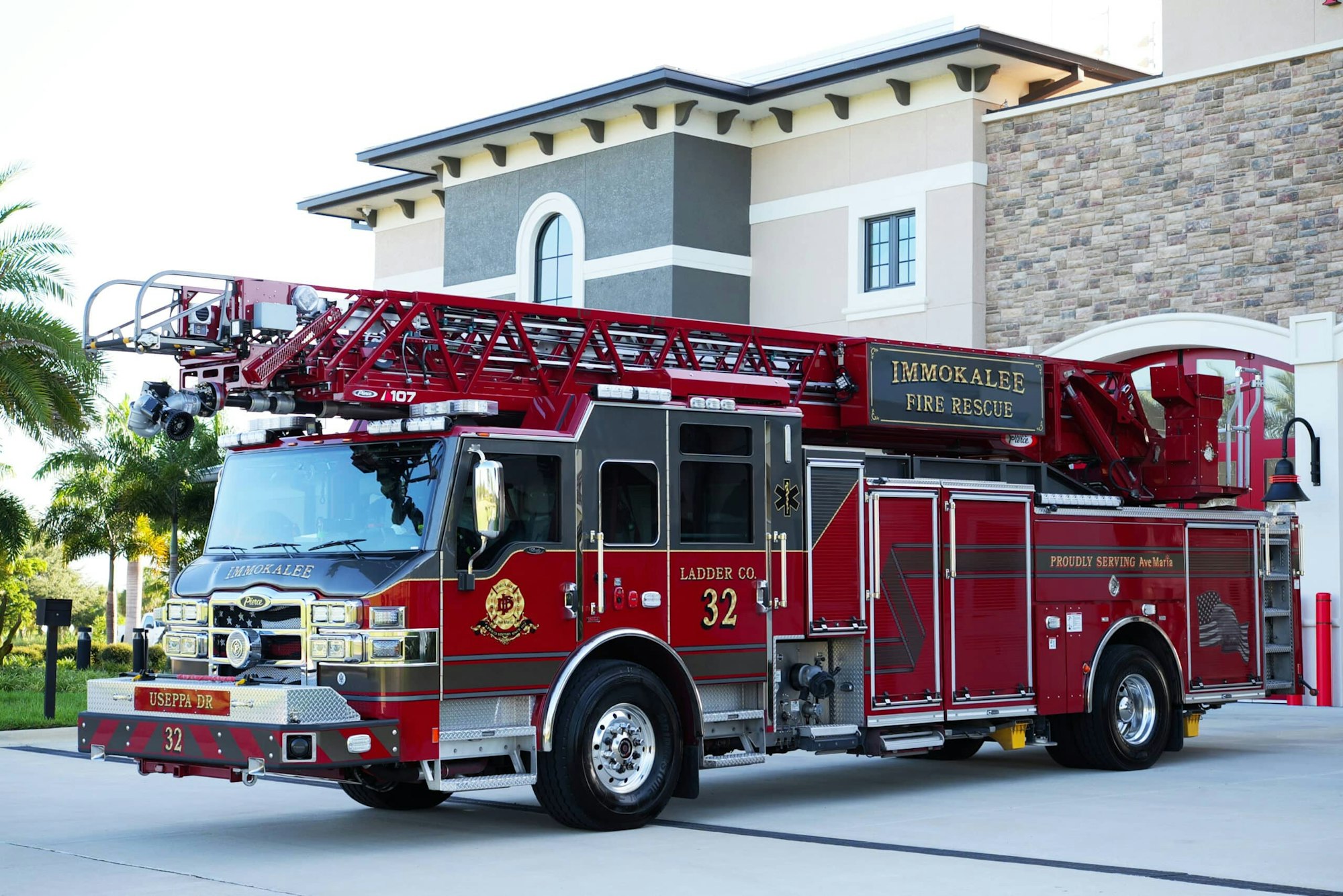 Red fire truck with an extended ladder, "Immokalee Fire Rescue," parked in front of a building.
