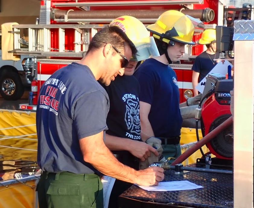Firefighters in uniform, examining equipment and papers near a fire truck.
