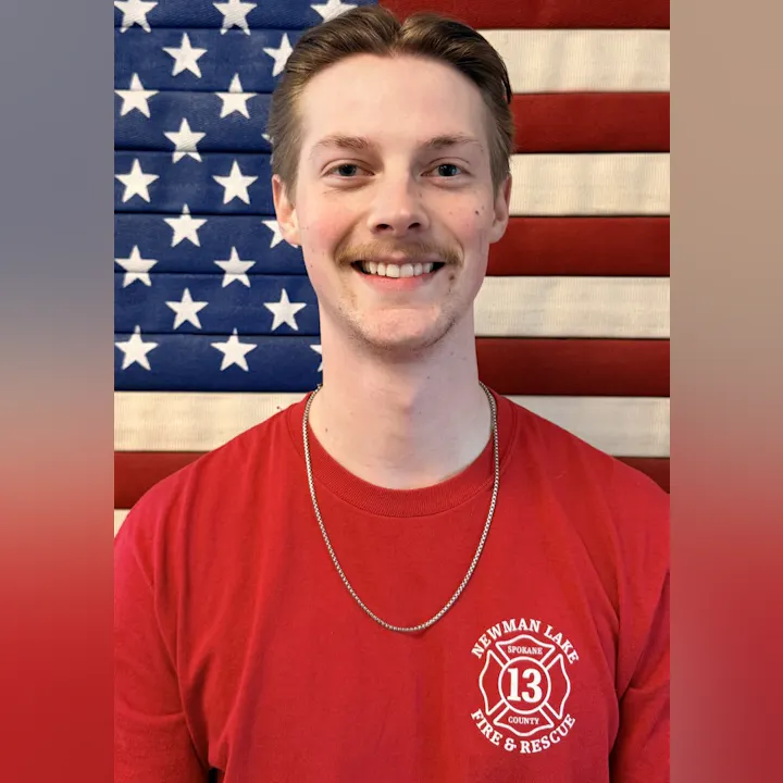 The image features a smiling individual in a red shirt with a fire department logo, set against an American flag backdrop.