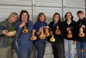 A group of six people smiling, holding decorated gourds.