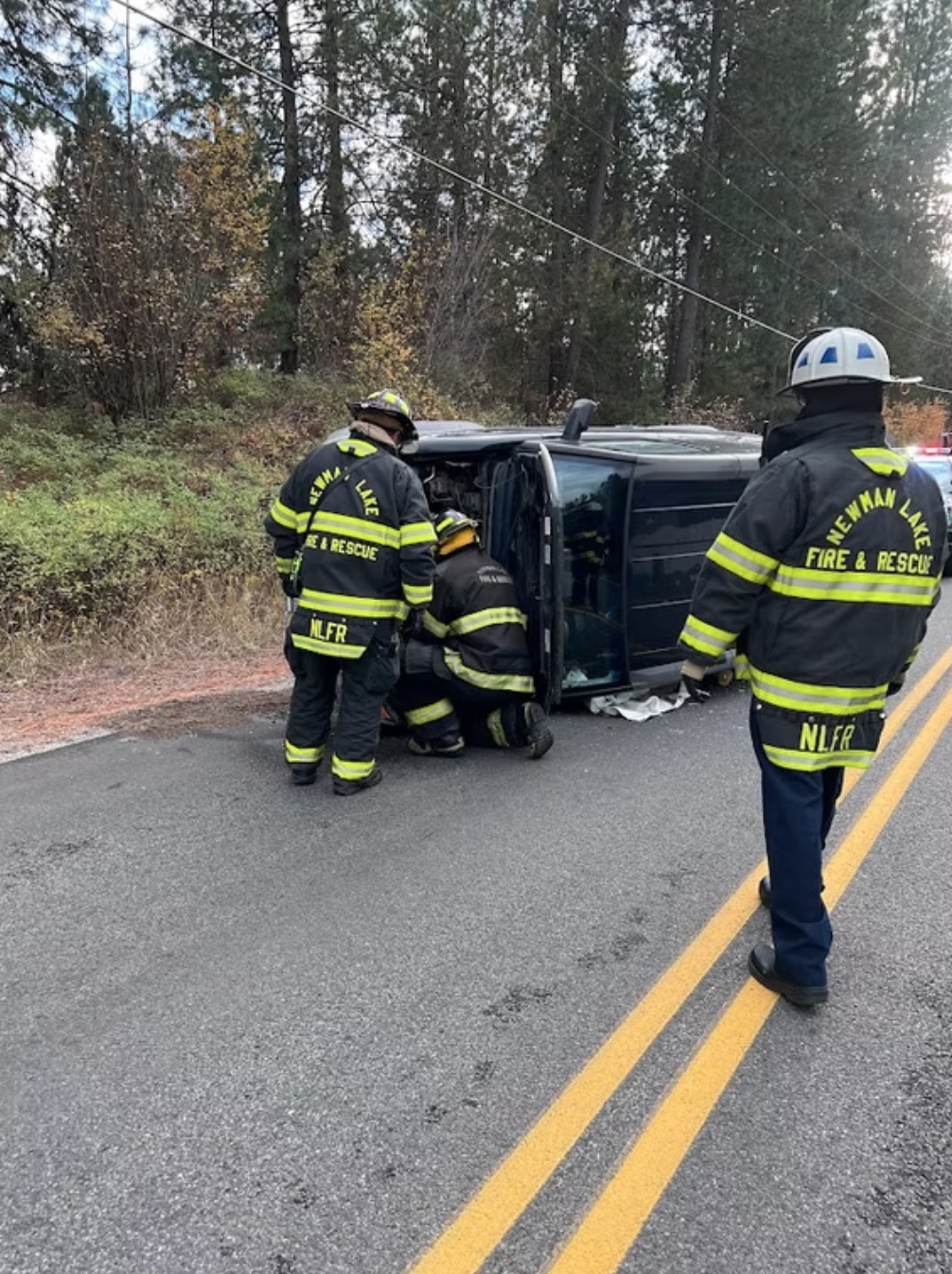 Firefighters assist at the scene of a vehicle on its side on a road.