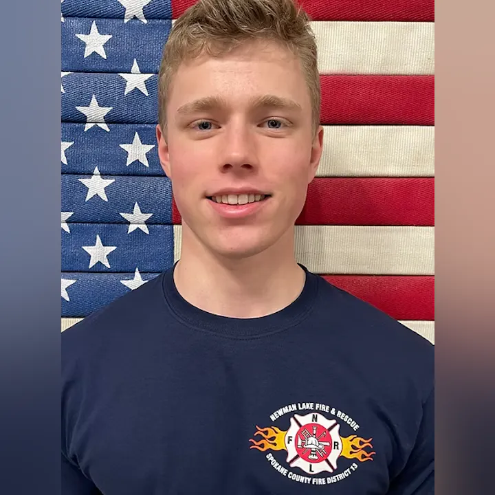 Person wearing a Newman Lake Fire & Rescue shirt, standing in front of an American flag backdrop.