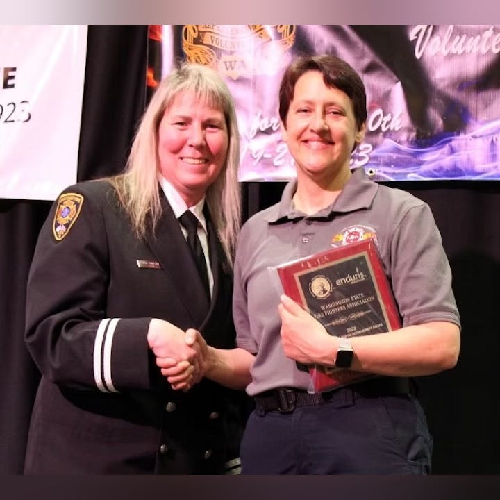 Two people are shaking hands; one is in uniform, the other holding a plaque at an award event.