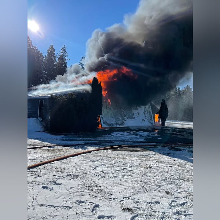 A building engulfed in flames and thick smoke on a snowy day, with fire hoses on the ground.