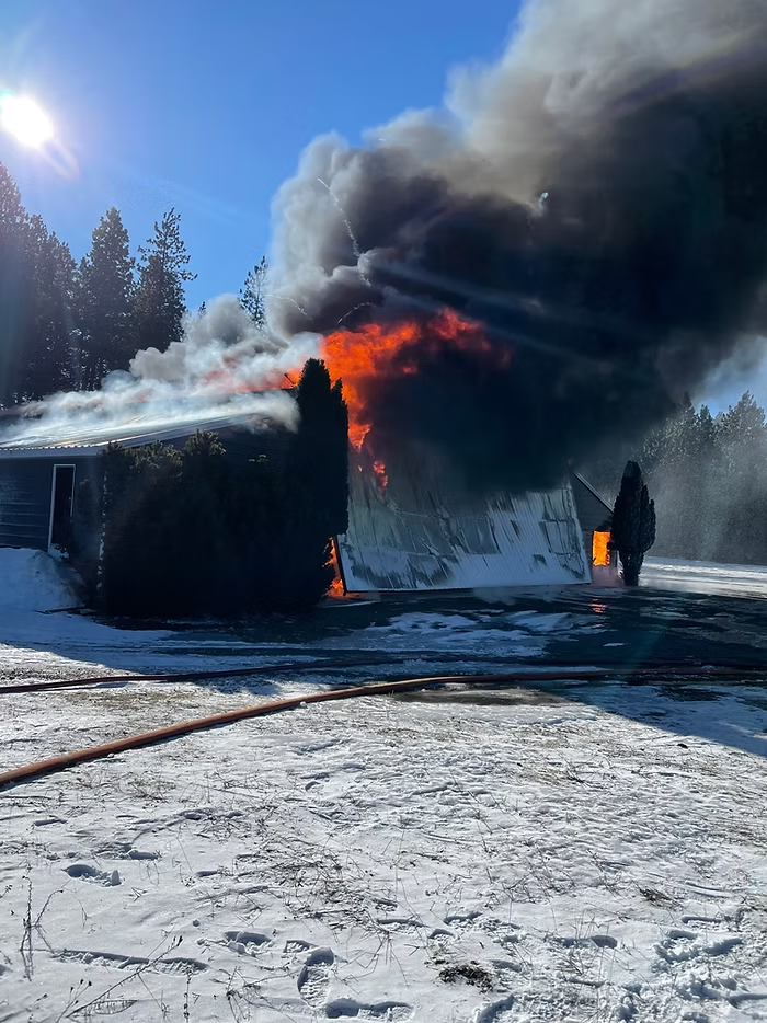 A building engulfed in flames and thick smoke on a snowy day, with fire hoses on the ground.