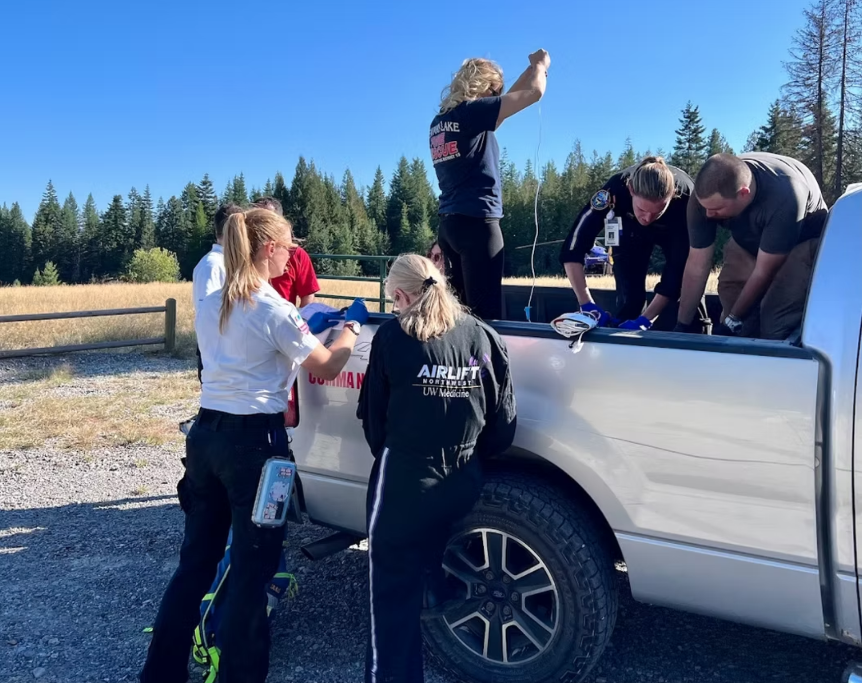 A group of emergency responders attending to a situation in the back of a pickup truck in a rural outdoor setting.