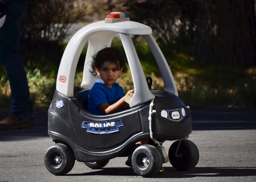 A child in a toy police car on a street.
