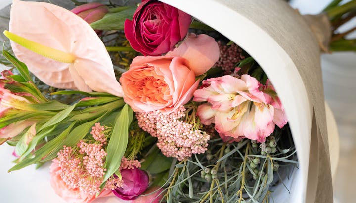A colorful bouquet of mixed flowers, including roses and an anthurium, in a white container.
