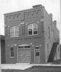 A two-story brick building with arched windows, a large garage door, and an external staircase.