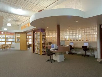 A spacious library with computers, bookshelves, and seating areas, featuring modern design elements and ample natural light.