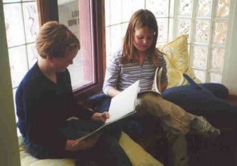 Two children sitting by a window, reading books together.