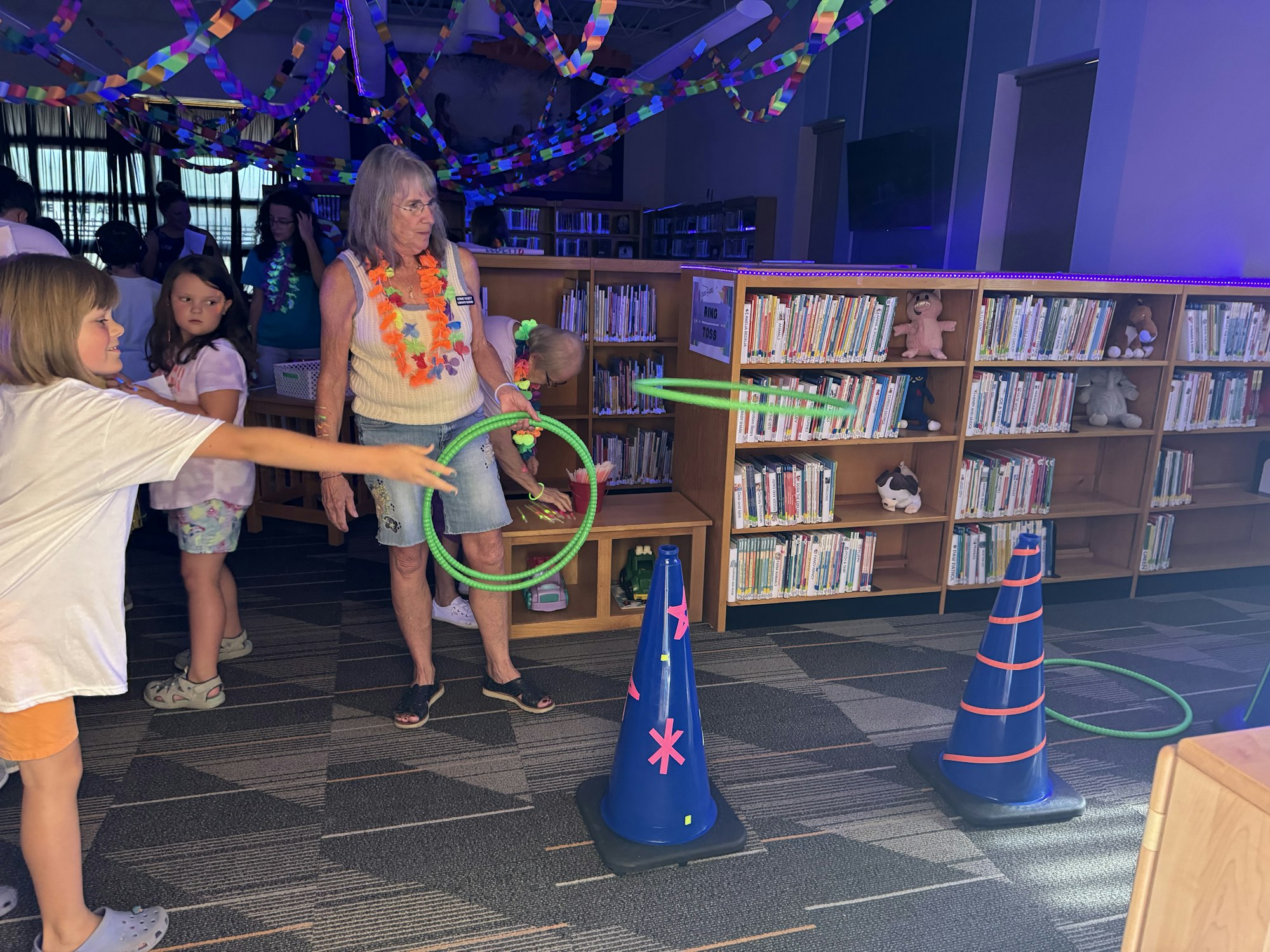Children and adults in a colorful library space, playing with rings; bookshelves in the background.