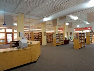 A library interior with bookshelves, a reception desk, and overhead lighting.