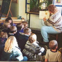 A teacher reads a book to a group of young children seated on the floor.