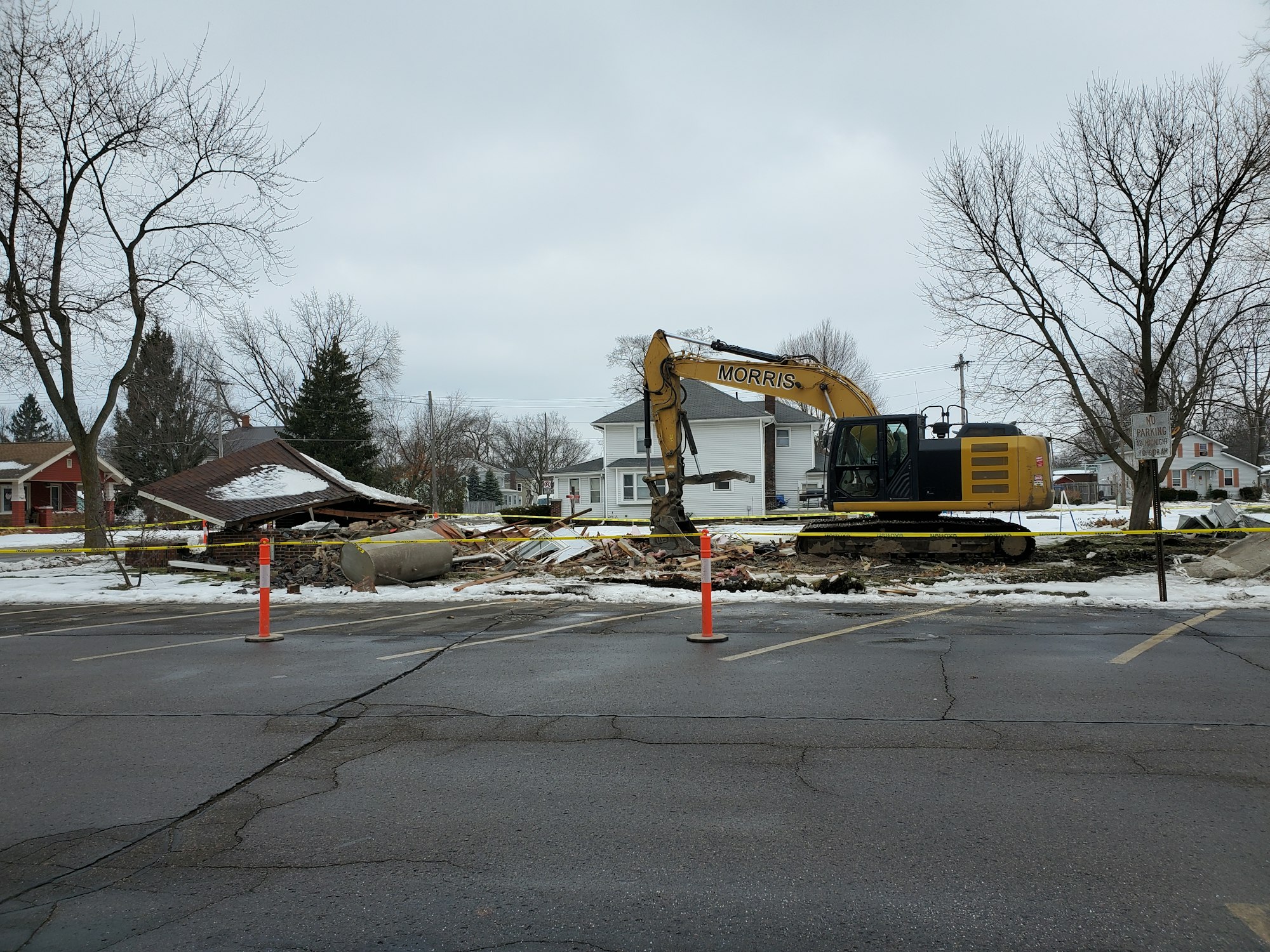 A construction scene featuring a demolished building, an excavator, and safety cones in a snowy area.