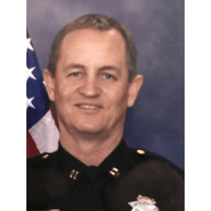 A smiling person in uniform with an American flag in the background.