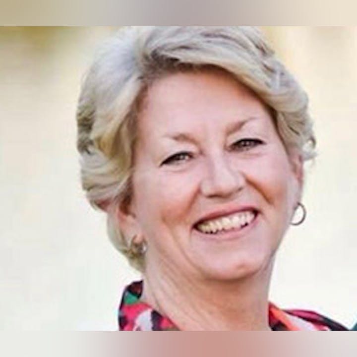 A smiling woman with short blonde hair, wearing earrings and a colorful top.