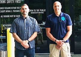 Two men standing in front of glass doors with safety signs.