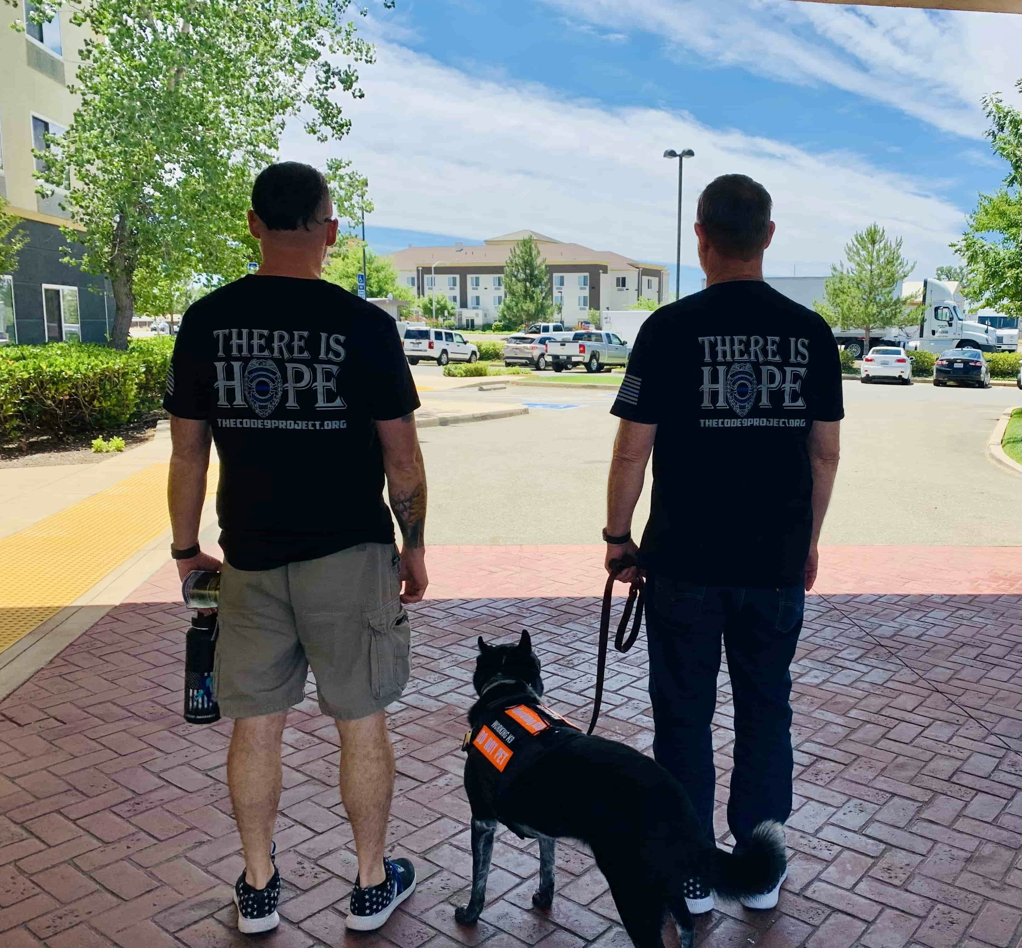 Two men with "THERE IS HOPE" shirts and a service dog outside a building.