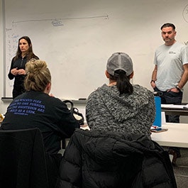 A classroom scene with two instructors at the front and students facing them, engaged in learning.