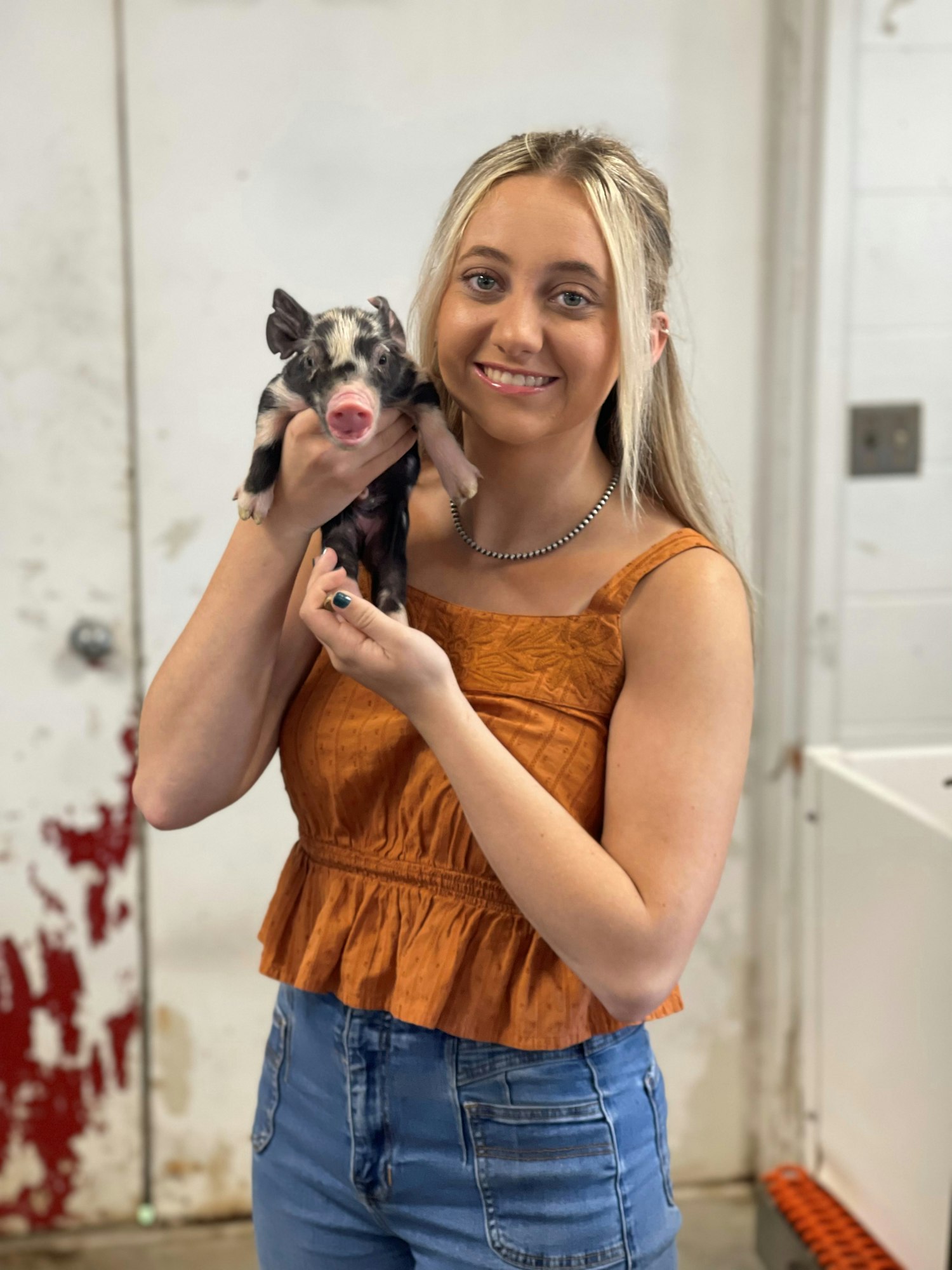 A smiling person holding a small piglet.