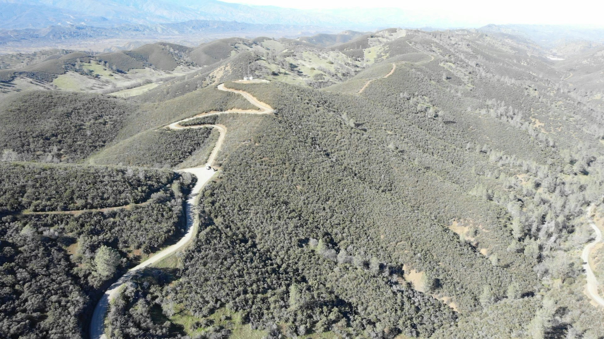 Aerial view of winding roads through hilly, wooded terrain.