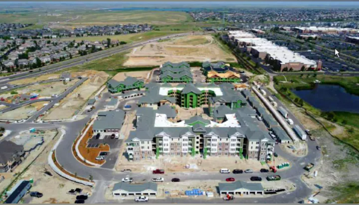 Aerial view of a suburban development with apartment buildings under construction, roads, and a pond.
