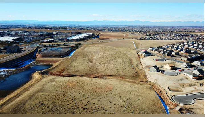 Aerial view of suburban development with houses, roads, and plains, against a backdrop of distant mountains.