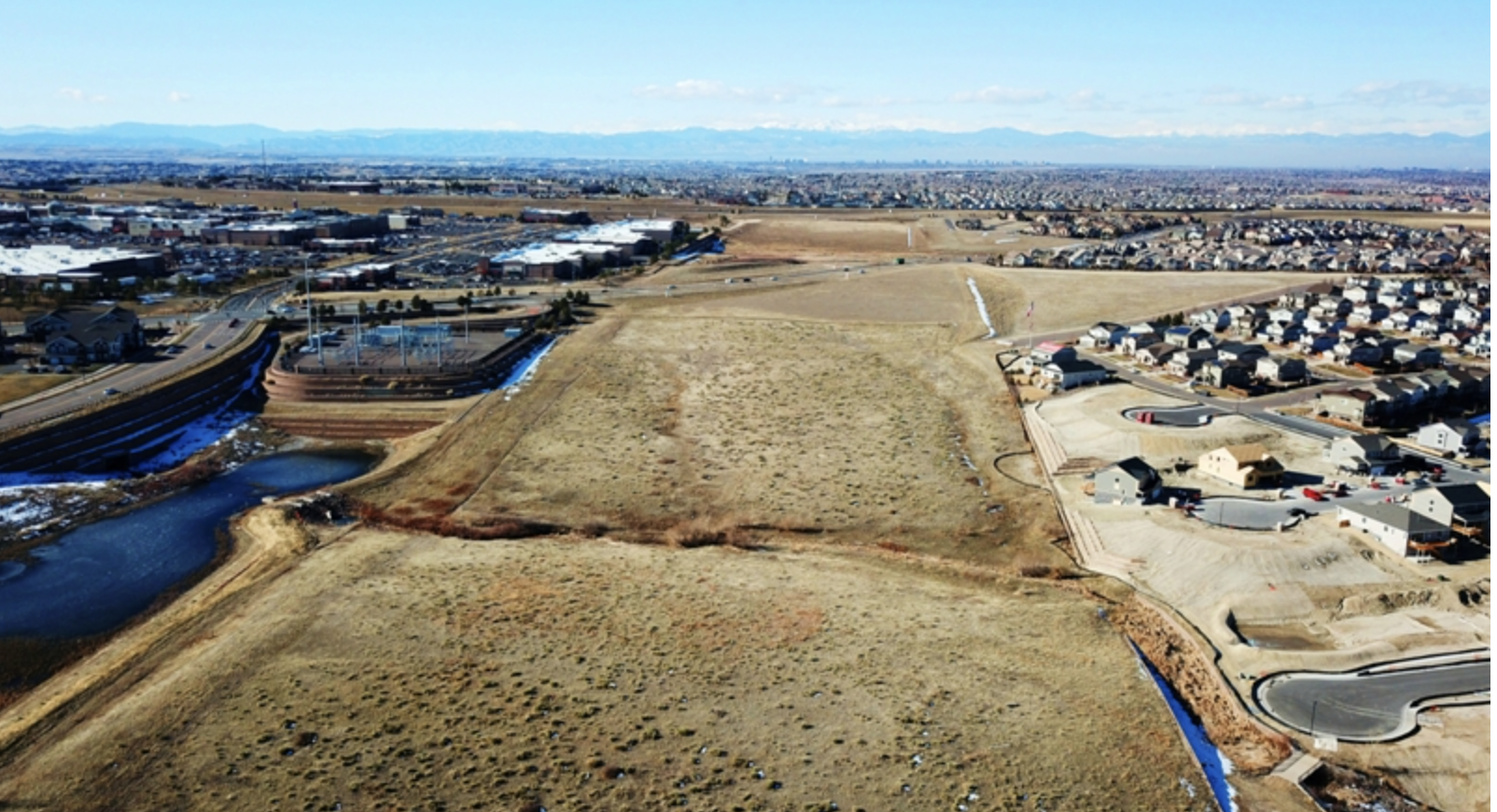 Aerial view of suburban development with houses, roads, and plains, against a backdrop of distant mountains.