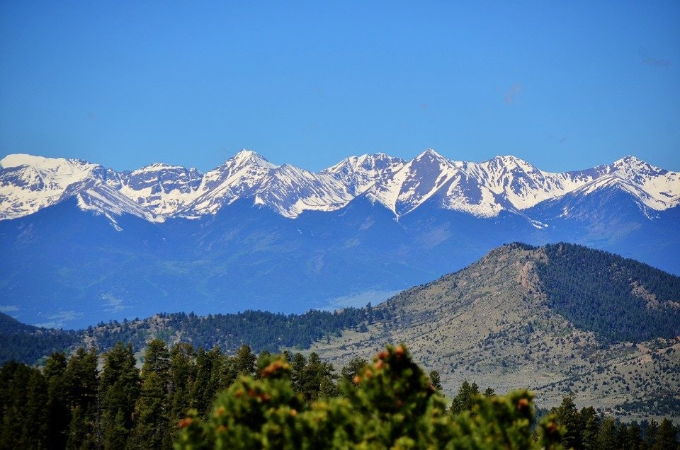 Snow-capped mountains behind rolling hills under a blue sky.