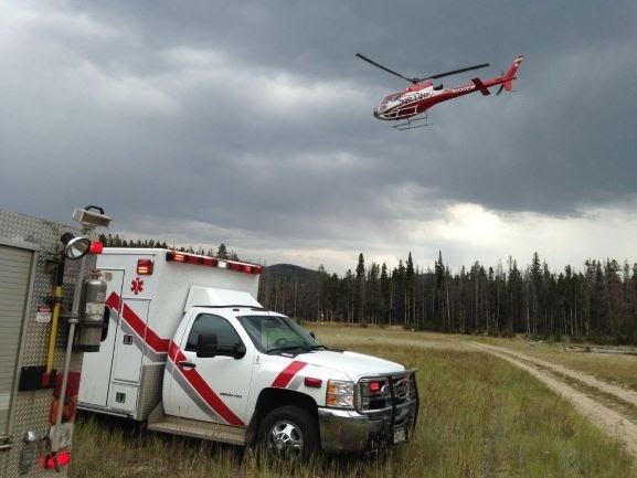 Ambulance and helicopter in a forest clearing under overcast skies.