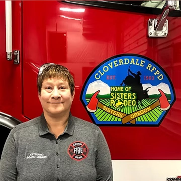 A person stands in front of a Cloverdale RFPD fire truck, featuring a logo for Sisters Rodeo, Oregon.