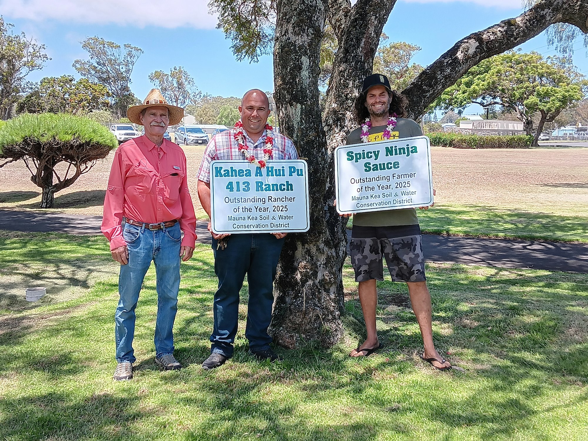 Three people stand holding award signs for outstanding rancher and farmer of the year 2025 from Mauna Kea Soil & Water District.