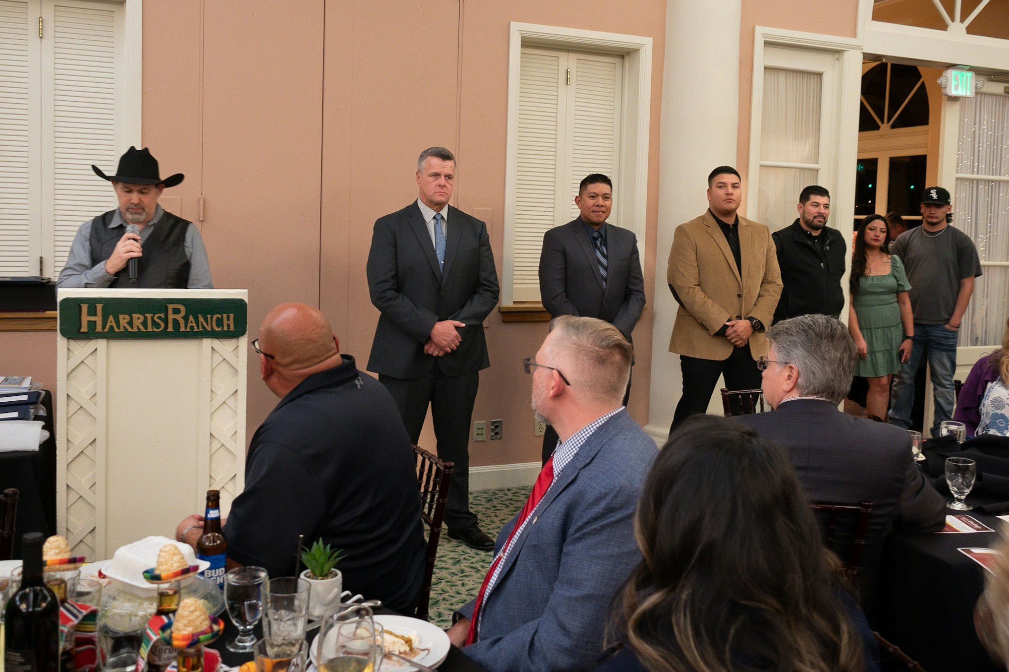 A speaker at a podium with onlookers at a formal event in a dining room.