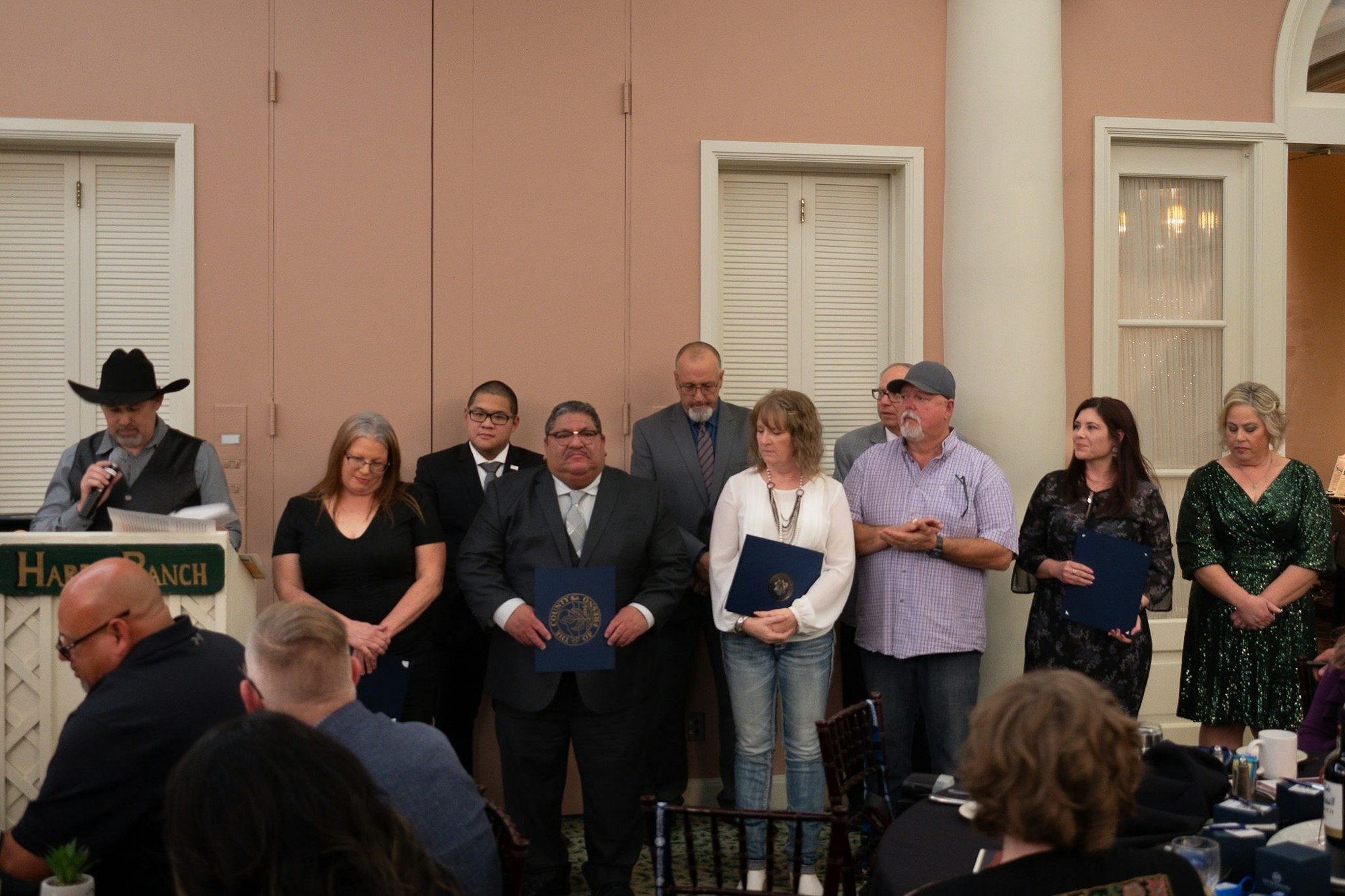 A group of people with certificates at an event, one person speaking at a podium.