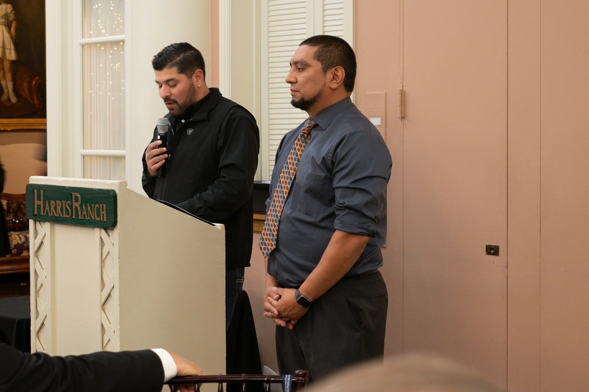 Two men at a podium, one speaking into a microphone. "Harris Ranch" is on the podium.