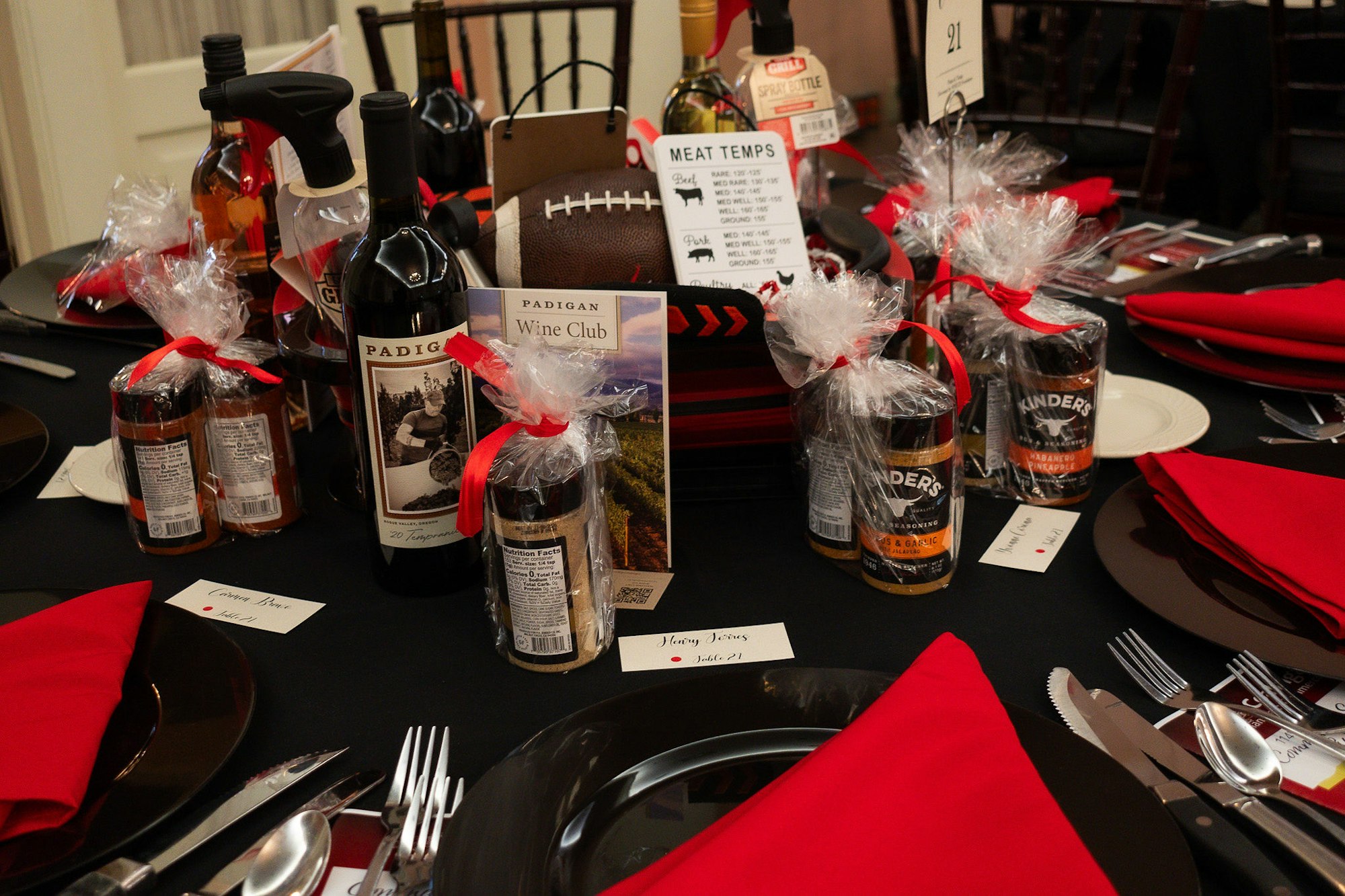 Dinner table with wine, gifts, name cards, and red napkins, possibly prepared for a special event.