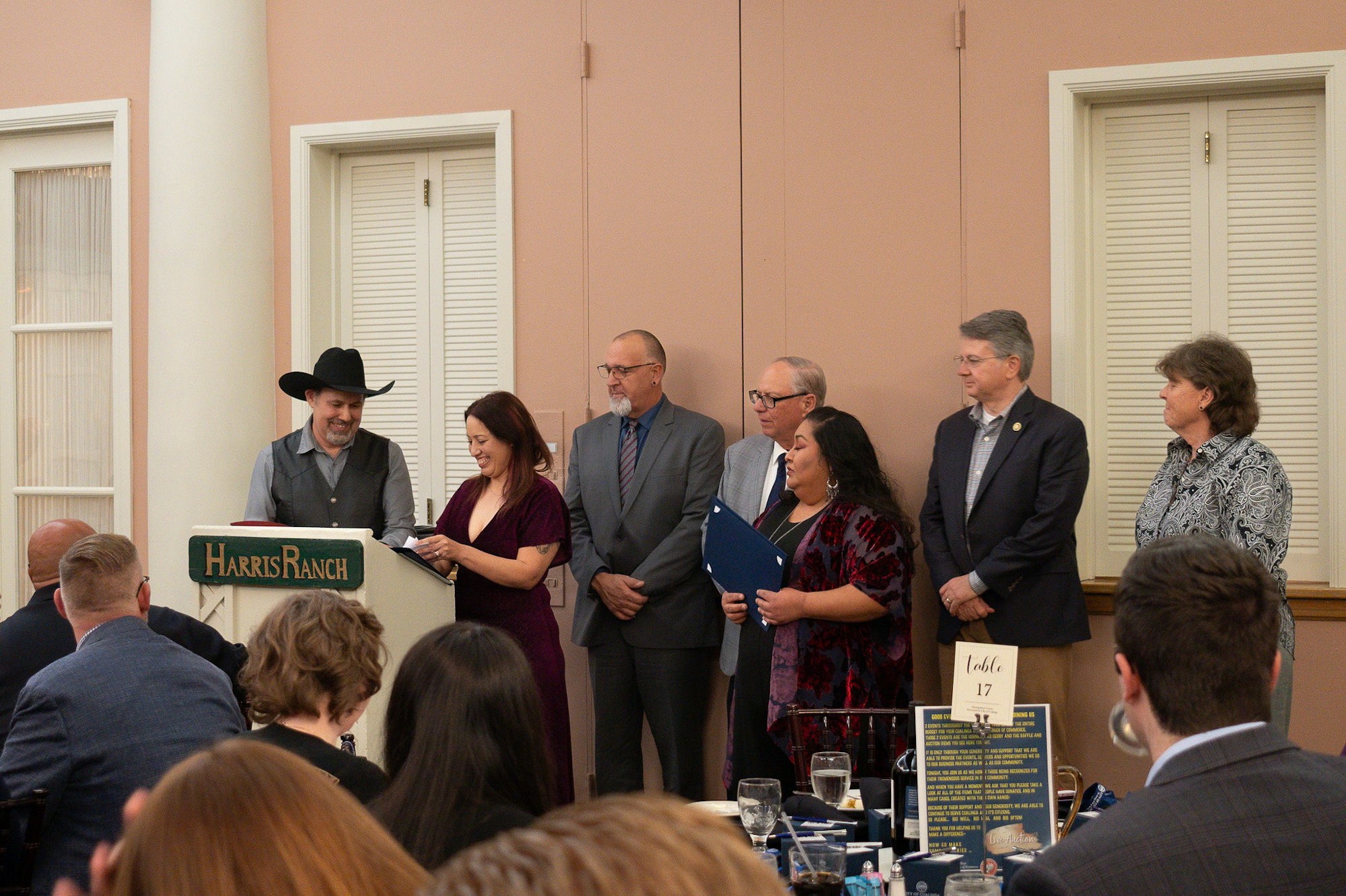 A group of individuals at a formal event, standing near a podium labeled "Harris Ranch."