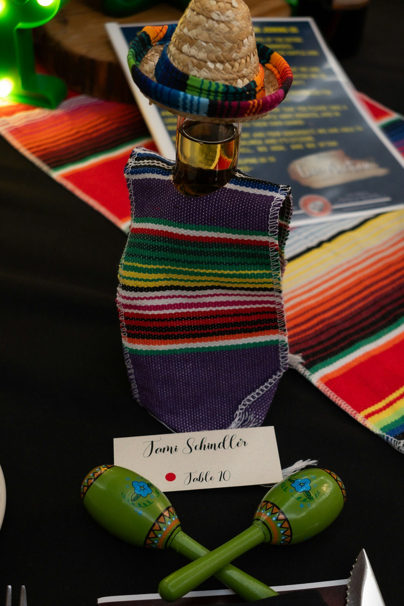 Colorful Mexican-themed table setting featuring a sombrero on a glass, maracas, and a name card.