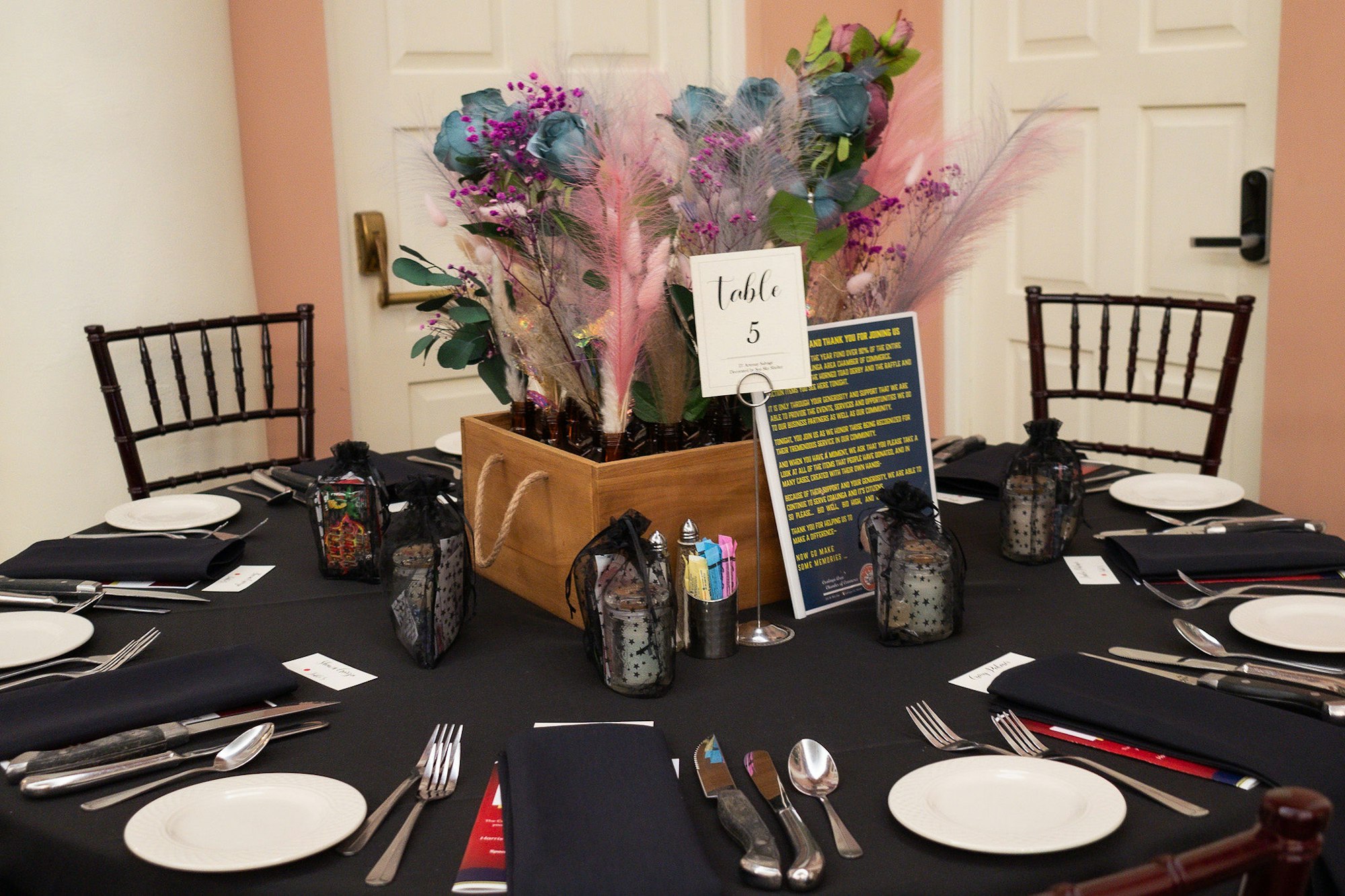 A decorated table set for an event with plates, cutlery, a floral centerpiece, and a "Table 5" sign.