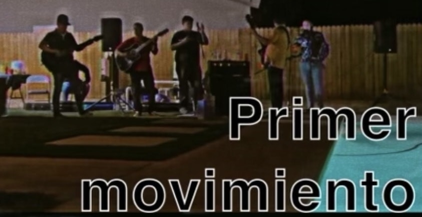 The image shows a band performing outdoors at night, with "Primer movimiento" displayed prominently.