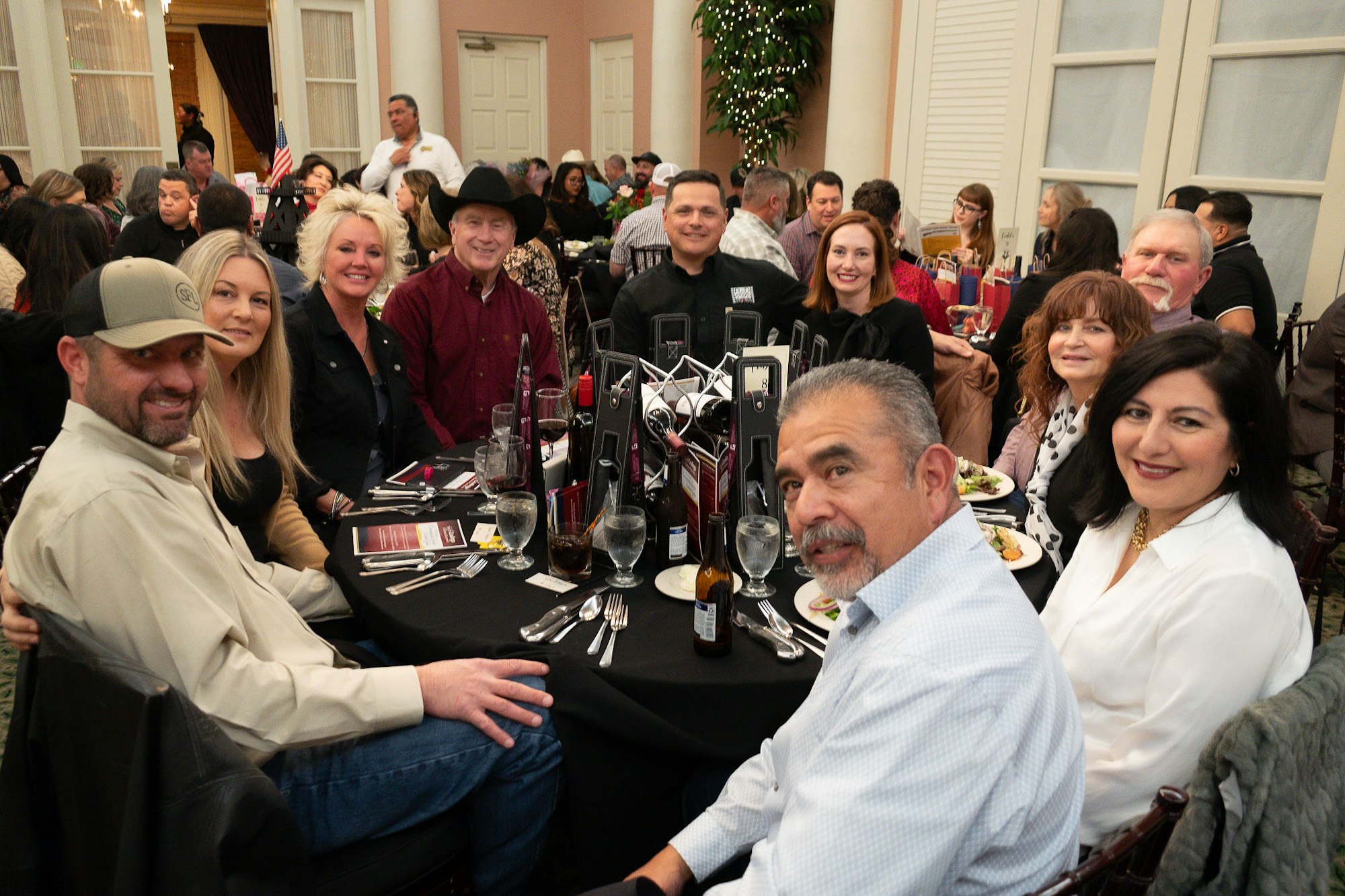A group of people smiling at a table during a social event with food and drinks.
