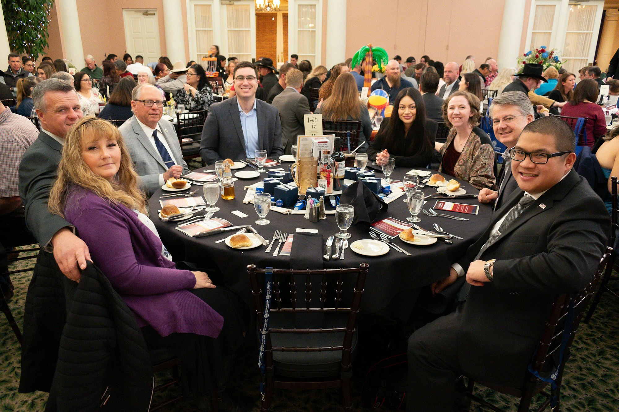 People sit at a decorated table in a banquet hall, smiling at the camera.