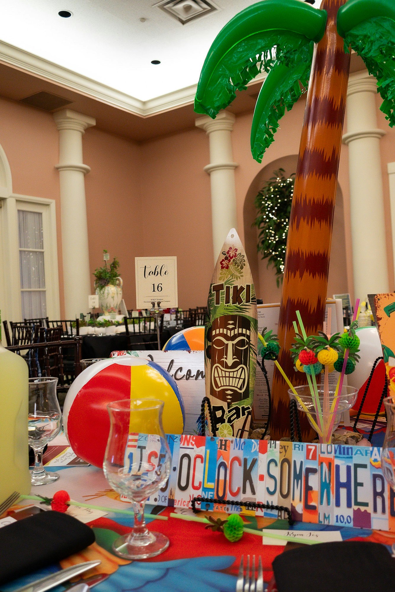 A festive table with beach-themed decor: inflatable palm tree, beach ball, Tiki sign, and a "5 o'clock somewhere" placard.