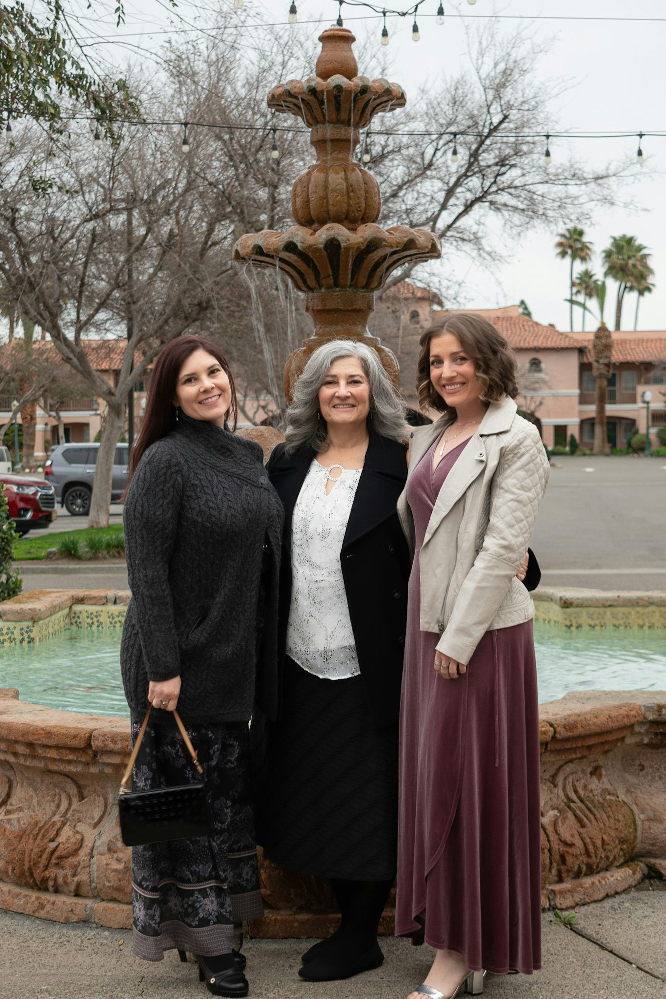 Three smiling women posing in front of a fountain.