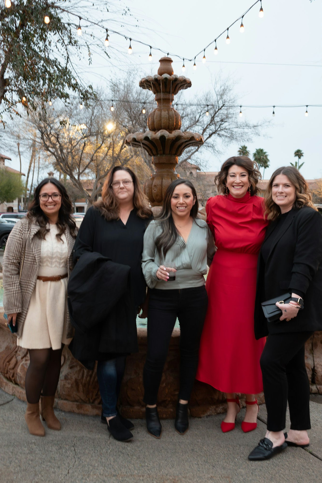 Five people posing with a fountain behind them and string lights above.