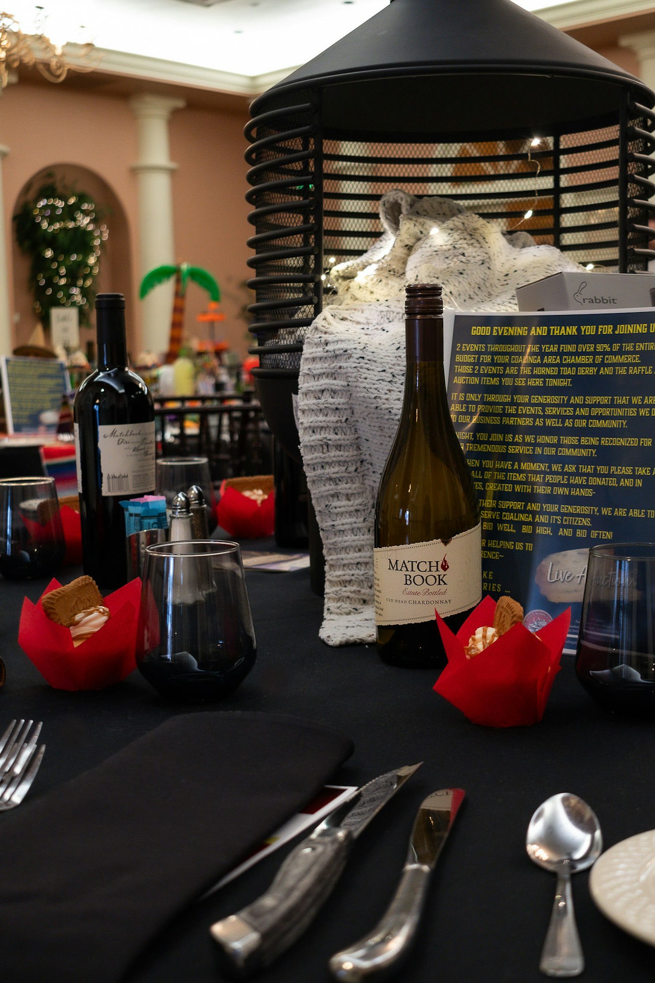 An elegantly set dinner table with wine bottles, glasses, and a menu, with a sculpture and decorations in the background.